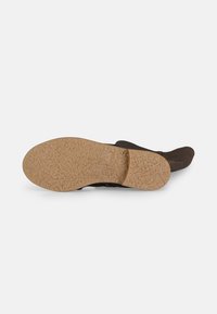 Sandal nera con una suola marrone texturizzata, caratterizzata da un design a strap intrecciato. Il materiale superiore sembra morbido, mentre la suola è resistente e antiscivolo.