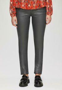Zwarte, slim-fit leren leggings met een gladde textuur, gecombineerd met chunky zwarte loafers. De top heeft een rood, slangenprintpatroon.