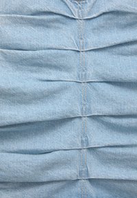 Ljusblå denimtyg med vertikala veck och synliga sömmar som skapar en texturerad känsla.
