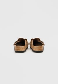 Bruna mockaskor i slip-on-modell med rund tå, justerbar rem, texturerad yta och en kontrasterande svart gummisula.