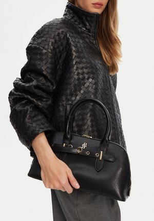 Mujer con una chaqueta de cuero negra texturizada sosteniendo un bolso de cuero negro con detalles dorados y doble asa.