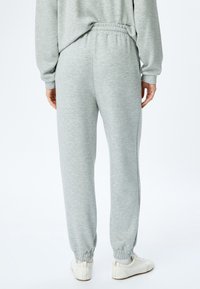 Lichtgrijze sweatpants gemaakt van zachte stof, met een elastische tailleband en boorden. Het ontwerp heeft een subtiele gemeleerde textuur.