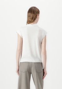Top blanco de manga corta con escote redondo, combinado con pantalones gris claro que tienen bolsillos traseros y costuras en contraste.
