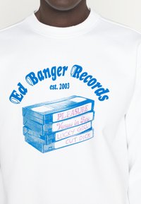 Felpa bianca con un design grafico di cassette impilate. Il testo blu recita "Ed Banger Records est. 2003" con titoli di diversi colori.