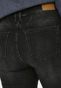 Melni denim džinsi ar gludu tekstūru, divām aizmugurējām kabatām un ar zīmola brūnu ādas uzlīmi jostā.