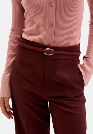 Geribbelde roze cardigan met knopen, gecombineerd met bordeauxrode broek met een slank riempje versierd met een gouden ovale gesp.