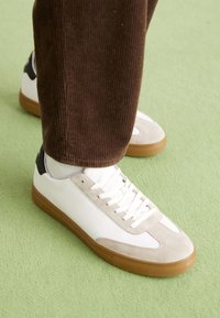 Baskets blanches et beiges en suède et cuir, avec un design à lacets, une semelle en caoutchouc et un accent noir au talon.