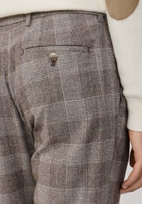 Braun karierte Hose mit strukturiertem Muster, einer hinteren Tasche mit Knopfverschluss und kontrastierenden beigen Akzenten an der Taille.