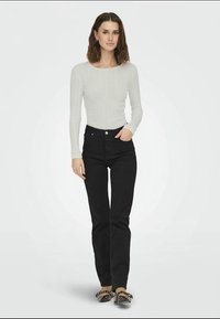 Helles graues, geripptes Langarmshirt, kombiniert mit hoch taillierten schwarzen Jeans und dunklen Schuhen. Einfaches, eng geschnittenes Design mit minimalen Akzenten.