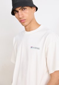 Hvid bomulds t-shirt med et lille, farverigt "CONVERSE" logo på brystet, korte ærmer og en afslappet pasform.