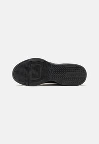Suela de zapatilla negra con goma texturizada, que presenta un dibujo en la banda de rodadura, logotipo de la marca y sección de puntera reforzada para mayor durabilidad.