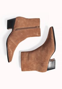 Bottes de cheville en daim marron avec une finition texturée, orteils ronds et un talon carré de hauteur intermédiaire. Présente une fermeture éclair sur le côté.