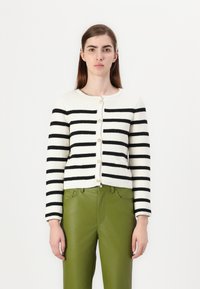 Svart og hvit stripete strikket cardigan med lange ermer, rund hals og seks gyldne knapper. Kombinert med grønne, tettsittende bukser.