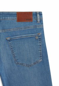 Blue denim jeans featuring a brown leather label with "BOSS." Includes a rear pocket with a silver accent logo and contrast stitching.