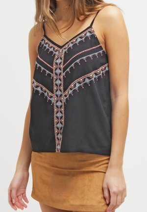 Mujer con un top negro sin mangas con bordado geométrico multicolor y una minifalda de ante color marrón claro.