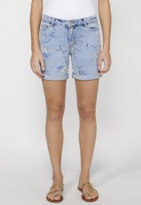 Shorts de denim azul claro con estampado floral, dobladillo enrollado y cinco bolsillos. Combinados con sandalias marrones que tienen acentos dorados.