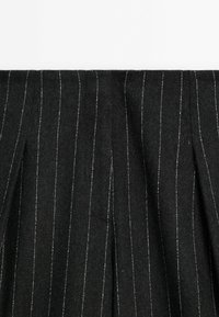 Black wool fabric with vertical white pinstripes, featuring a textured surface and pleated design.