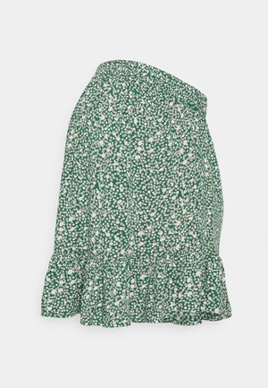 Grønt skørt med hvidt spredt prikkemønster, elastisk talje og flæsekant, vist fladt på en hvid baggrund.
