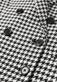 Materiał w biało-czarny wzór houndstooth z sześcioma czarnymi guzikami o gładkim wykończeniu, tworząc teksturowany wygląd.