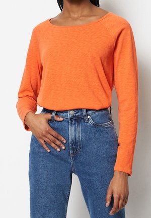 Haut à manches longues, col rond en orange vif, fabriqué en tissu doux et texturé. Associé à un jean en denim taille haute.