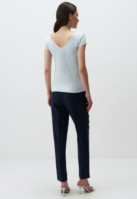 Jasnoniebieski prążkowany top z tyłem w kształcie litery V, w połączeniu z ciemnoniebieskimi spodniami o klasycznym kroju i metalicznymi sandałami na obcasie, na jednolitym białym tle.