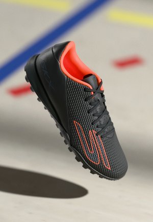 Black soccer shoes composed of textured synthetic material, featuring orange accents, lace-up design, and a studded rubber outsole.