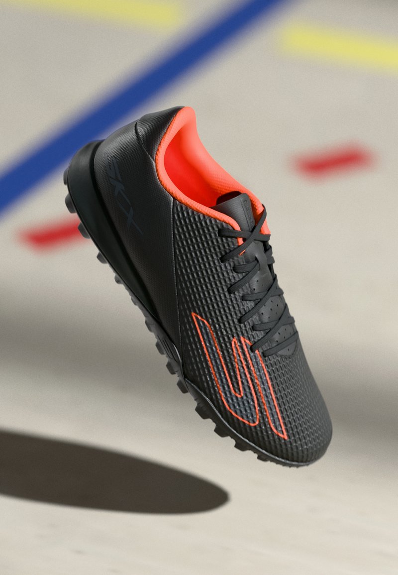 Black soccer shoes composed of textured synthetic material, featuring orange accents, lace-up design, and a studded rubber outsole.