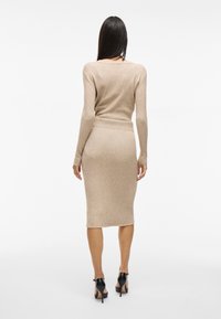 Ribbat stickad beige klänning med långa ärmar, kroppsnära passform, längd till mitten av vaddern och en mjuk textur, tillsammans med svarta högklackade skor.