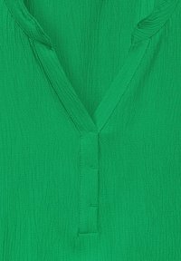 Blusa verde strutturata con scollatura a V e dettaglio a bottoni sul davanti. Il tessuto presenta un aspetto stropicciato e una finitura morbida.