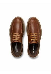 Scarpe di pelle marrone con punte tonde, solette marroni e lacci beige. Presentano cuciture bianche lungo le suole e un logo visibile sulla soletta.