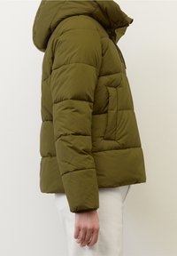 Olivgrön dunjacka med huva, med quiltad textur, sidoficka och en figursydd silhuett. Slätt syntetiskt material.