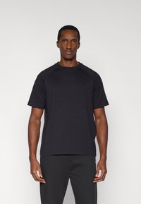 Μαύρο κοντομάνικο μπλουζάκι με στρογγυλή λαιμόκοψη και μανίκια ράγκλαν, κατασκευασμένο από απαλό, ελαφρύ ύφασμα. Διακριτική λεπτομέρεια με λογότυπο στο στήθος.