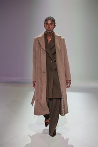 Cappotto in misto lana marrone con grandi rever, indossato sopra un completo marrone scuro a doppio petto e pantaloni a righe, abbinato a tacchi a punta.