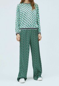 Maglietta a maniche lunghe con un motivo geometrico in tonalità di verde e blu, abbinata a pantaloni a gamba larga con una fantasia floreale su sfondo verde.