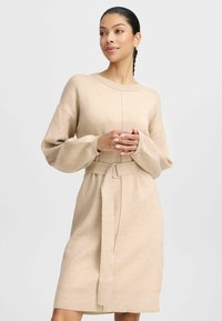 Beige Strickkleid mit langen, übergroßen Ärmeln, einem runden Ausschnitt und einer taillierten, mit einer Metallverschluss-Akzent versehenen Taille. Weiche Textur.