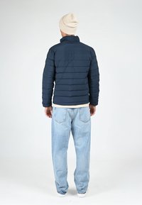 Doudoune bleu marine avec un design matelassé horizontal, col montant et tissu léger. Portée avec un jean ample bleu clair.