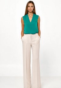 Bezrekawnik w kolorze turkusowym z dekoltem w serek, zestawiony z kremowymi, wysokim stanem spodniami wyposażonymi w przednie kieszenie i dopasowanym krojem.