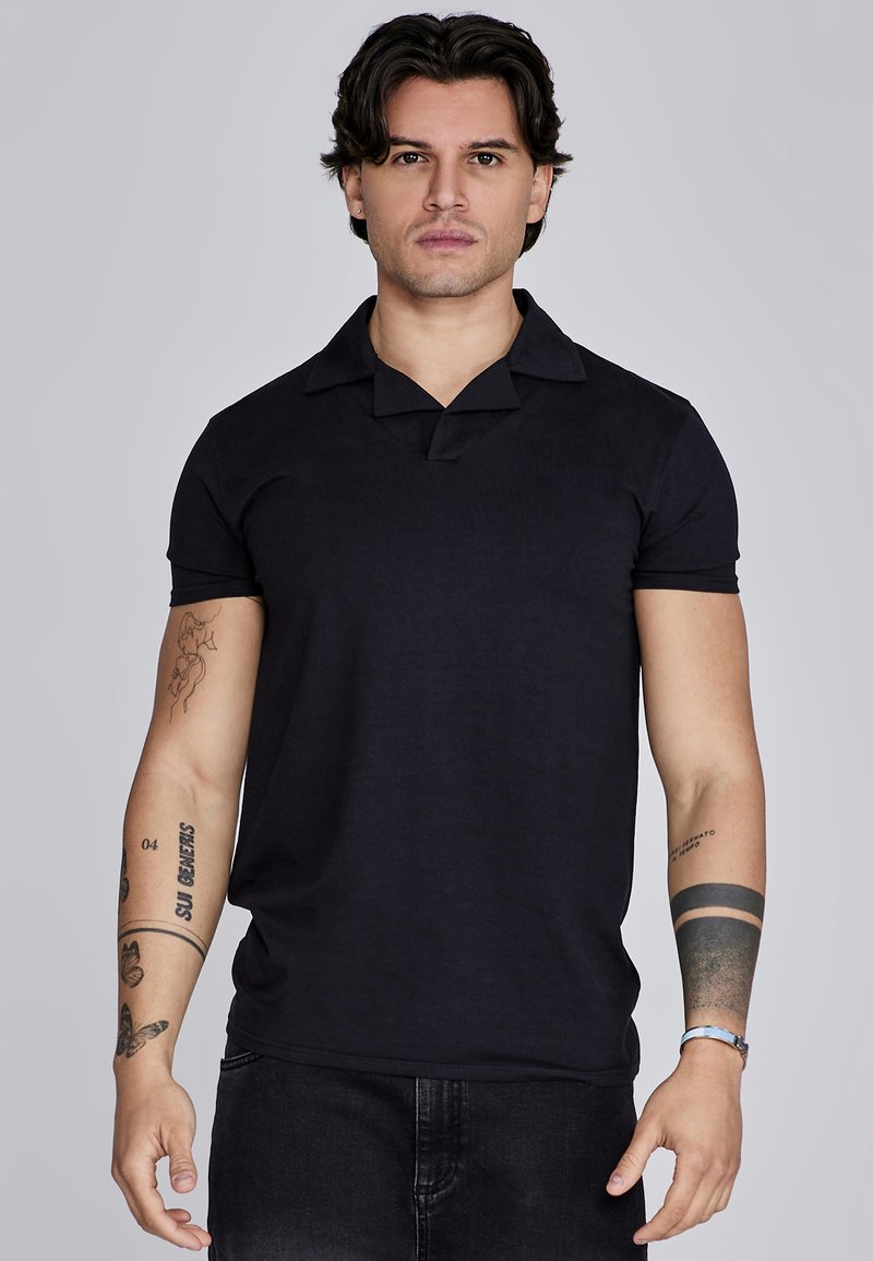 Čierna polokošeľa s krátkym rukávom, výstrihom do V a širokým golierom. Mäkká, rebrovaná textúra. Model má na sebe tmavé džínsy a vidieť mu tetovania na rukách.