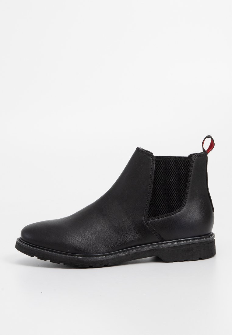 Bottine Chelsea en cuir noir avec des panneaux élastiques sur les côtés, un bout arrondi, un talon bas et une languette rouge à l'arrière. Semelle texturée pour une bonne adhérence.