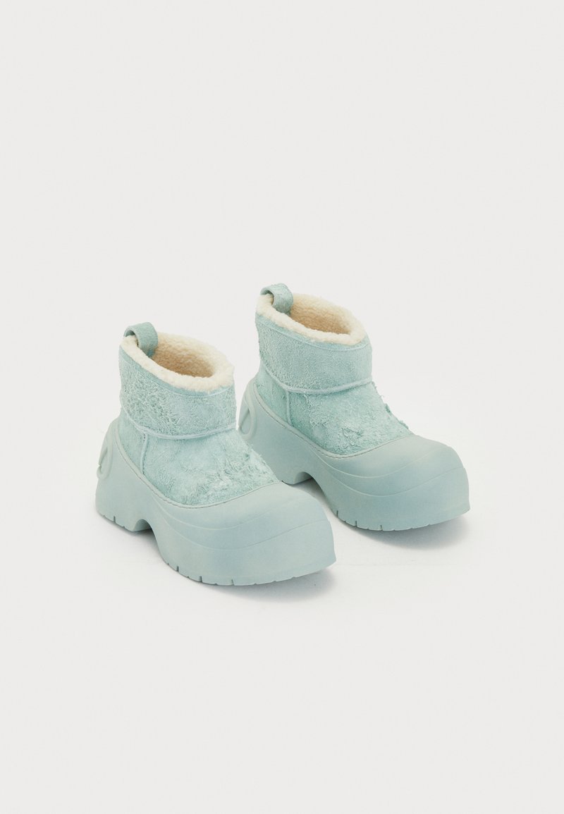 Hellblaue Knöchelstiefel mit einem weichen, flauschigen Innenfutter, strukturiertem Obermaterial und dicker Gummisohle. Verfügt über eine Zuglasche für einfaches An- und Ausziehen.