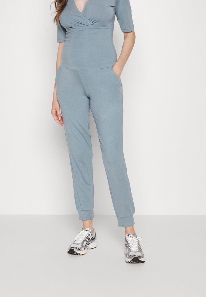 Svetle modrý, přiléhavý jogger set z měkkého materiálu. Tílko má design s překlápěním a krátké rukávy. Kalhoty obsahují boční kapsy.