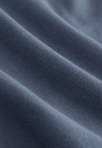 Sötétkék szövet, sima, puha textúrával, enyhe nyúlást és finom kötésmintát mutatva, lágy hajtásokkal és ívekkel.