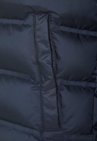 Gros plan d'une poche de veste matelassée noire avec un matelassage horizontal et des bords cousus.