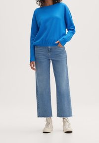 Niebieski sweter o fakturze dzianinowej, zestawiony z jasnoniebieskimi, wysokim stanem spodniami typu wide-leg i białymi trampkami. Stylizacja ma swobodny, luźny fason.