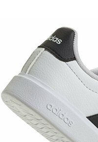 Baskets synthétiques blanches avec des accents en cuir noir, dessus texturé, col rembourré et logo en relief sur le côté. Semelle en caoutchouc épaisse.