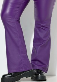 Fioletowe, sztuczne skórzane spodnie dzwony o błyszczącym wykończeniu, z starannie wykonanymi szwami i szerokimi nogawkami. Połączone z masywnymi, czarnymi butami na sznurówki.