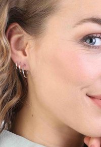 Silberne Creolen mit drei übereinander gestapelten Ringen in unterschiedlichen Größen, die mit einer glatten, polierten Oberfläche Licht reflektieren.