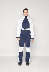 Tume sinine ja valge suuskade kostüüm, millel on lukuga eesmine osa, kapuuts, vöö talje juures ja tekstureeritud kangas, millel on peen disain.