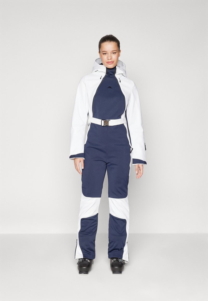 Tume sinine ja valge suuskade kostüüm, millel on lukuga eesmine osa, kapuuts, vöö talje juures ja tekstureeritud kangas, millel on peen disain.