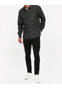 Ciemnoszara koszula na guziki z dwoma kieszeniami na piersi, długimi rękawami i dopasowanym krojem, w zestawieniu z czarnymi spodniami o slim fit i białymi trampkami.